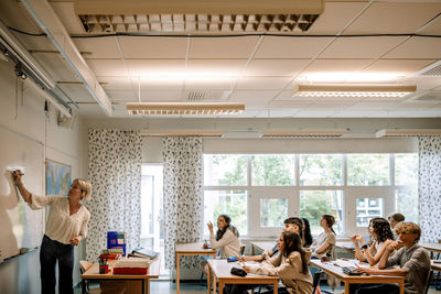 Female teacher teaching to girls and boys in illuminated classroom