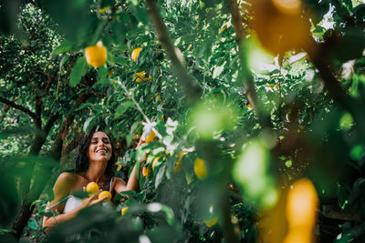 Young woman standing by tree against plants