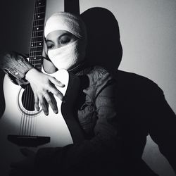 Young woman with face wrapped in textile holding guitar against wall
