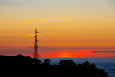 Silhouette electricity pylon by tree against romantic sky at sunset