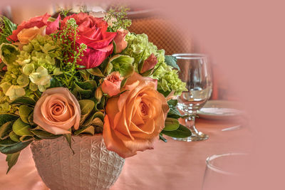 Pale peach roses, green hydrangea, and pink roses in a bouquet on a table display for dinner.