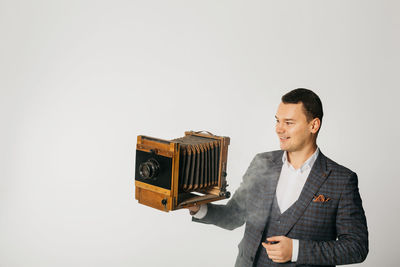 Man holding camera while standing against white background