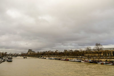 Boats moored at harbor against sky in city