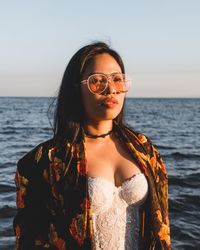 Beautiful young woman wearing sunglasses against sea at beach