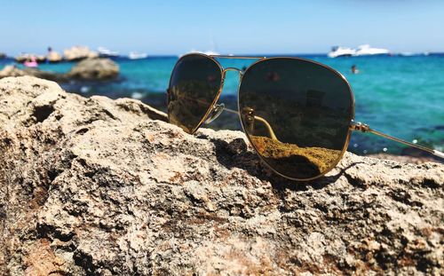 Close-up of sunglasses on rock at beach against sky