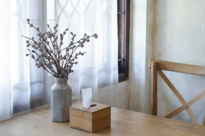 Flower vase on table against window at home