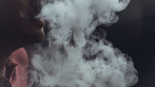 Close-up of man smoking against black background