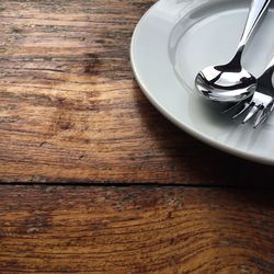 Close-up of fork and spoon on plate over wooden table