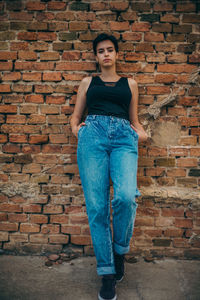 Portrait of young woman standing against brick wall