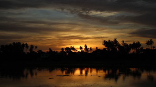 Silhouette trees by lake against sky during sunset