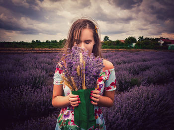 Young woman holding flowers on field against sky during sunset