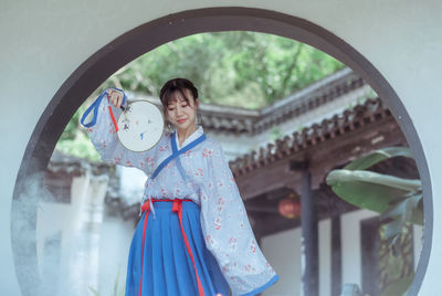 Young woman holding umbrella while standing in mirror