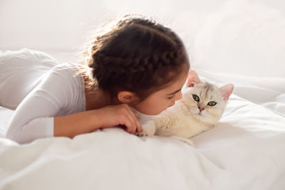 Portrait of a beautiful little girl, lies on a clean, white bed with a white british cat.