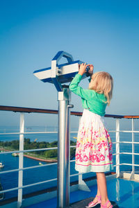 Girl standing by coin operated binoculars against sky