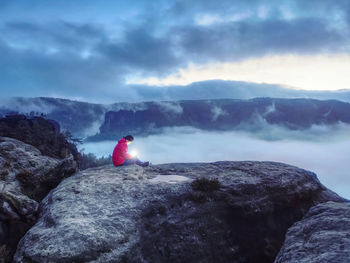 Lost girl sit on rocky peak in darkess holding in hands symbol of hope. unfaithfulness, magic love