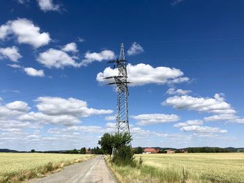 Electricity pylon on field by road against sky