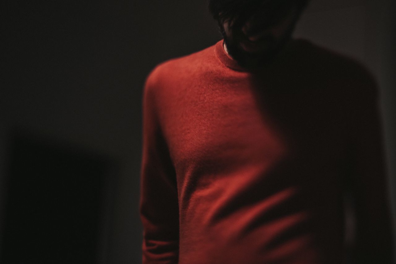 one person, indoors, standing, red, front view, waist up, studio shot, dark, men, casual clothing, young adult, midsection, real people, lifestyles, copy space, adult, young men, black background, contemplation