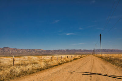 Road amidst field against blue sky