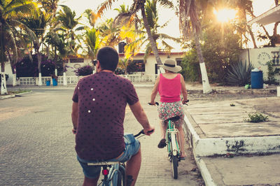 Man and woman riding bicycles at sunset with palm trees