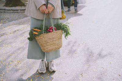 Hands of woman holding bag of vegetables standing on footpath