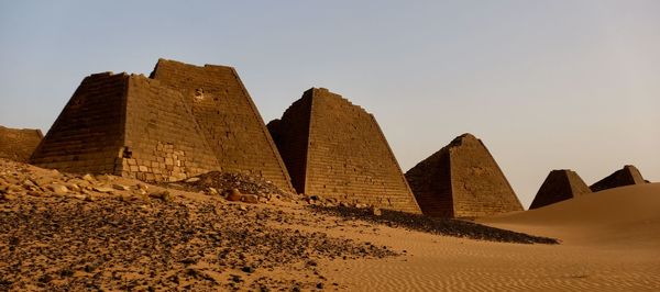 Damaged pyramids at desert against clear sky during sunset