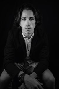 Portrait of young man sitting against black background