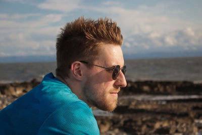 Close-up of man wearing sunglasses looking away while sitting against sea