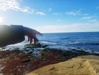 Close-up of hand by sea against sky