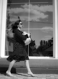 Side view of woman with arms raised standing against window