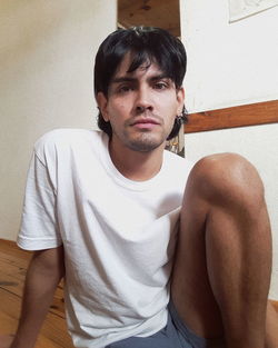 Portrait of young man sitting against wall at home