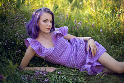 Teenage girl with dyed purple hair and a nose piercing in the grass and in a short dress