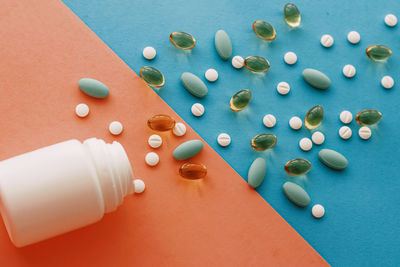 High angle view of pills spilling from bottle against blue background