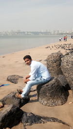 Full length of man on rock at beach against sky