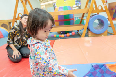 Cute girl with teacher on carpet in kindergarten