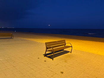 Empty bench on beach against sky at night