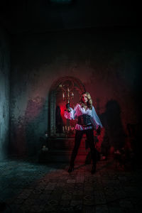 Woman in costume holding candle while standing at abandoned building during night