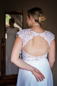 Rear view of young woman in a wedding dress standing in front of a mirror 