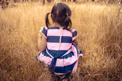 Rear view of girl crouching on grassy field