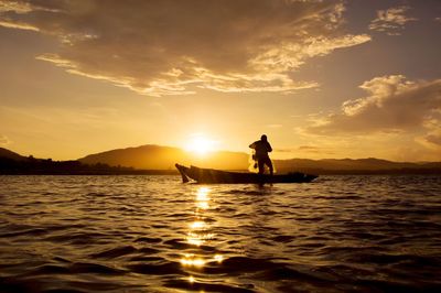 Silhouette man in sea against sky during sunset