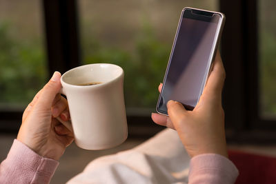 Close-up of hand holding coffee cup on table