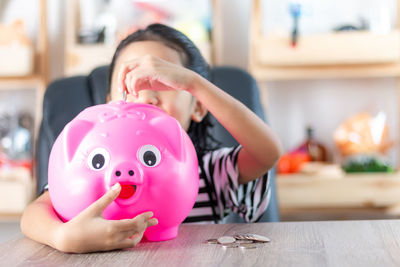 Girl putting coin in piggy bank at home