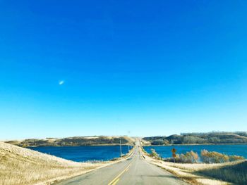 Road amidst land against clear blue sky