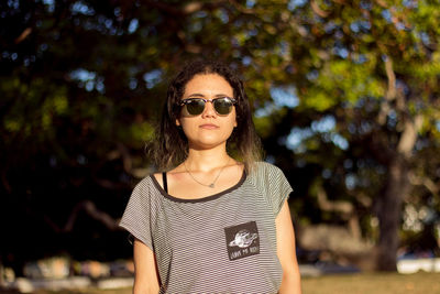 Portrait of young woman wearing sunglasses standing against trees