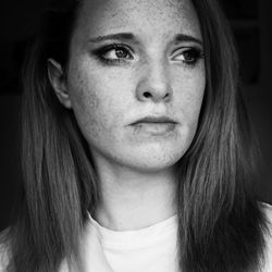 Close-up of young woman looking away standing against black background