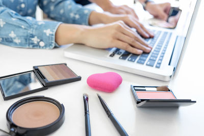 Midsection of woman with beauty product using laptop at table