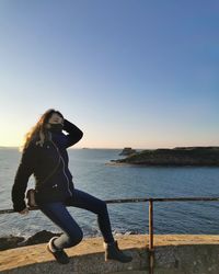 Woman on railing against sea against clear sky