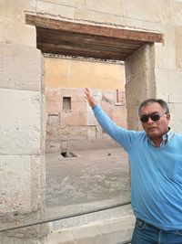 Young man wearing sunglasses standing against wall