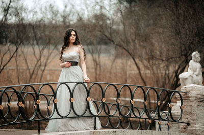 Woman sitting on railing against trees