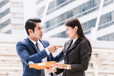 Colleagues discussing while standing against buildings in city