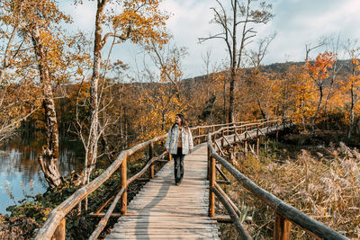 Portrait of young adult woman walking on wooden path in forest in autumn.